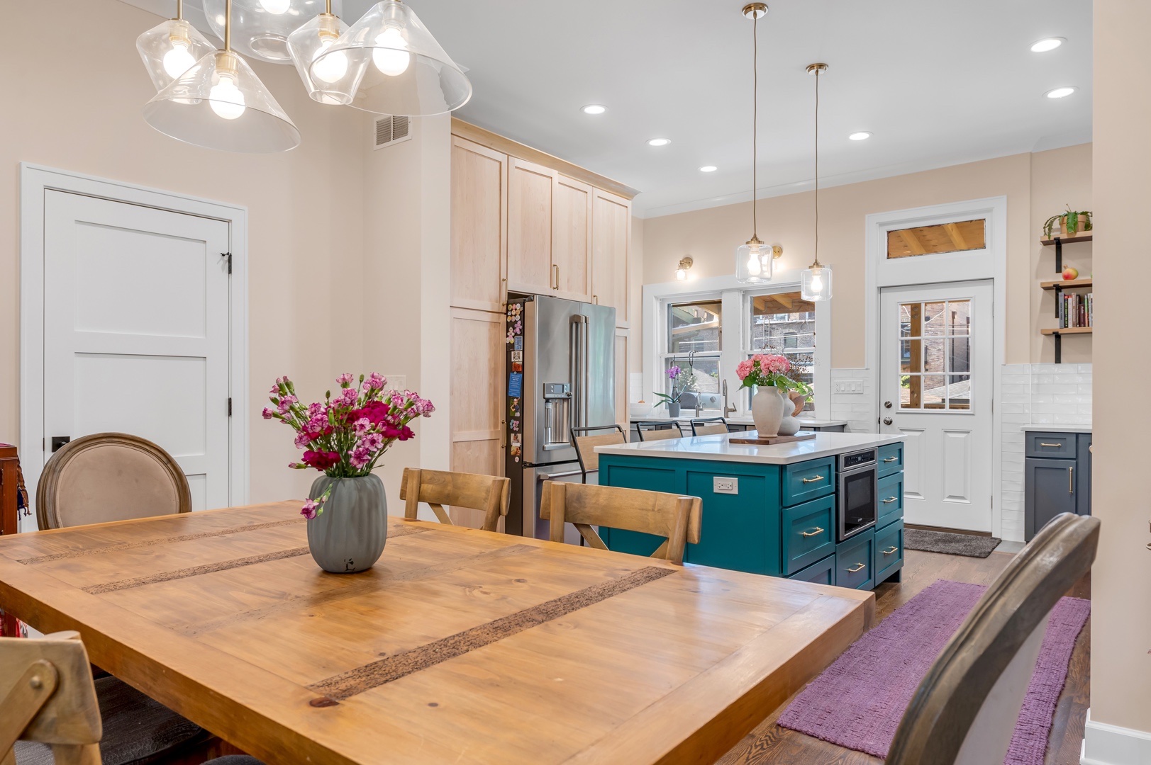 Image of fully remodeled kitchen with light fixtures above windows, open shelving, subway tile, quartz countertops, blue island cabinets, and brass hardware.