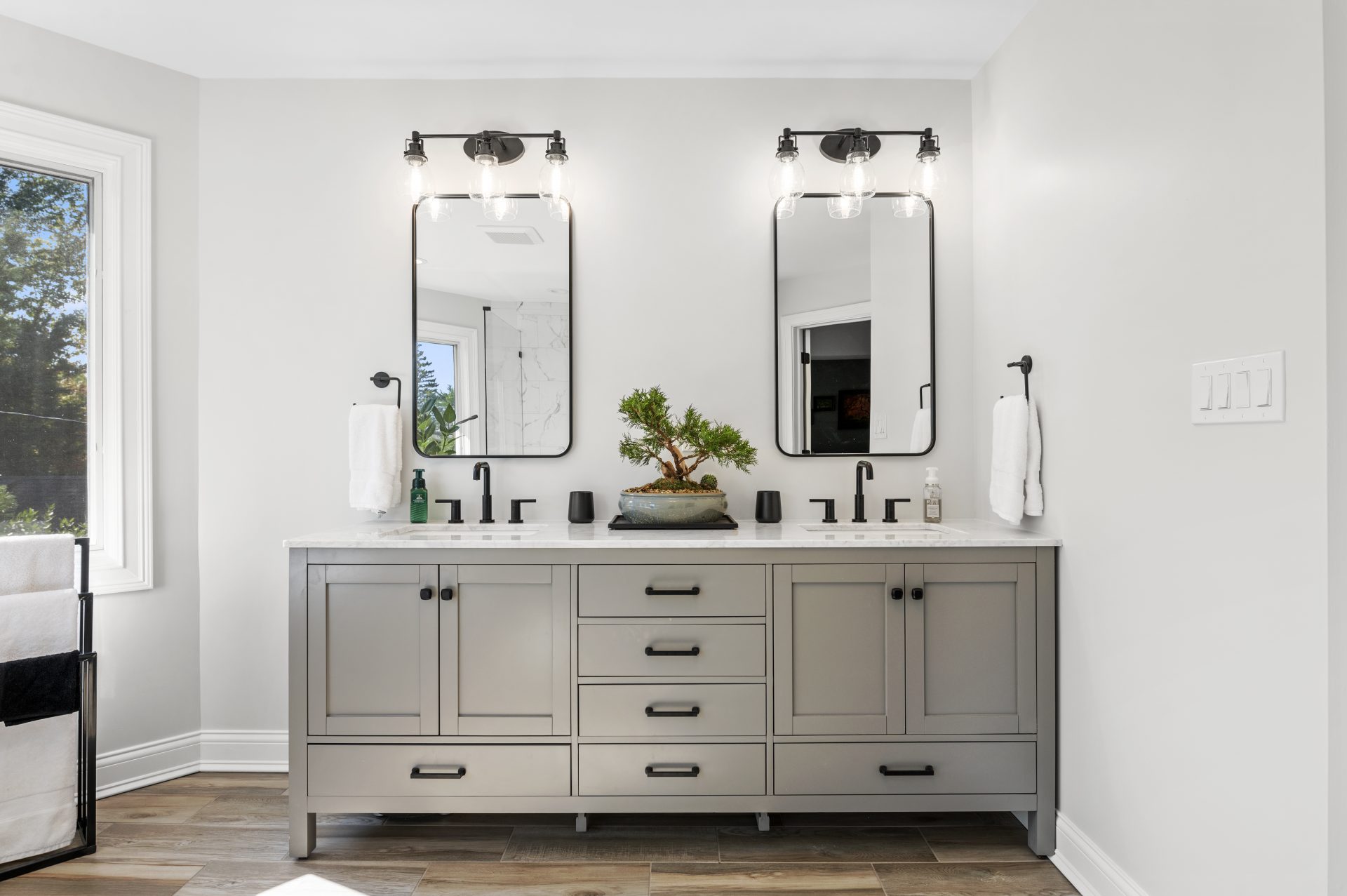 Remodeled master bathroom with a double sink vanity, two mirrors, black fixtures, tiles that look like hardwood, and two light fixtures