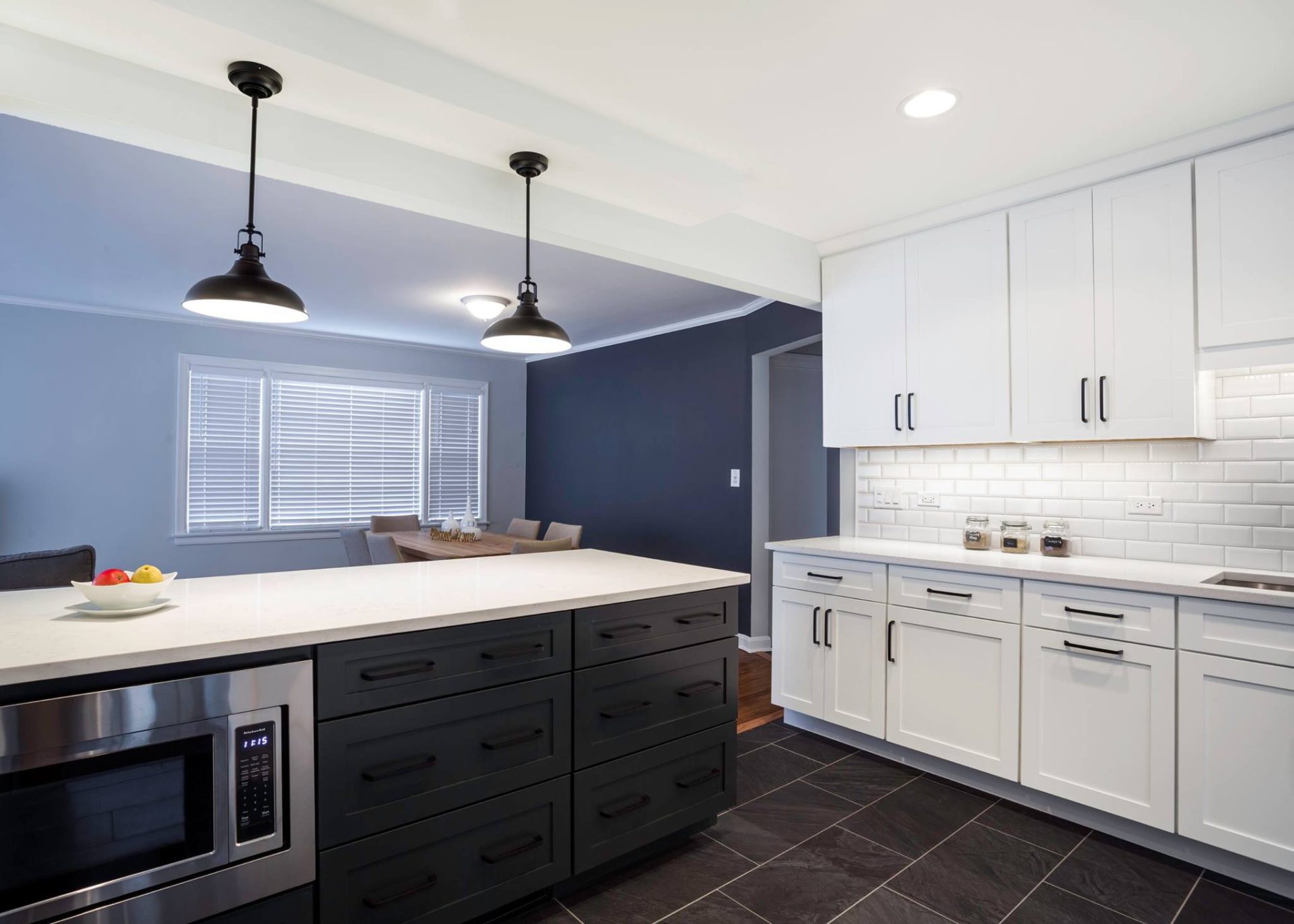 Full kitchen remodel with two tone cabinets, black hardware, black matte faucet, white quartz, white subway backsplash tiles, stainless steel appliances, peninsula, pendants above peninsula, can lights, large floor tiles, build-in microwave in peninsula