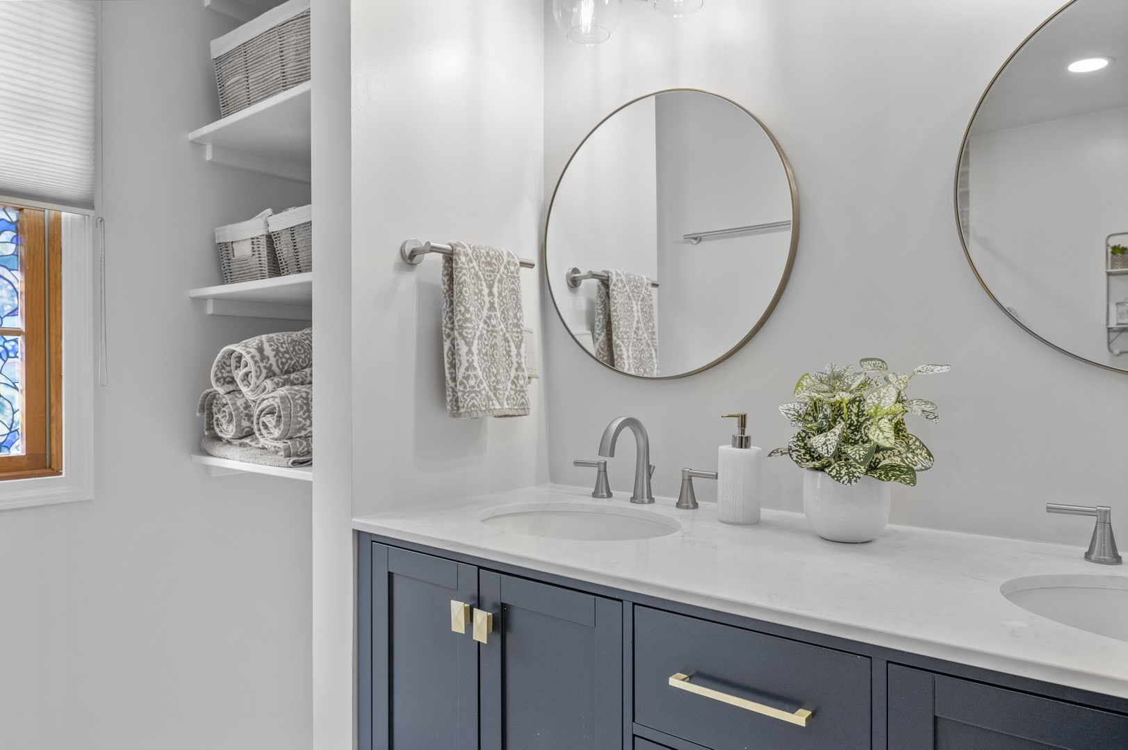 Remodeled bathroom with a double sink navy vanity, two mirrors, two gold light fixtures, chrome accessories, chrome faucets, closet with open shelving, and large floor tiles