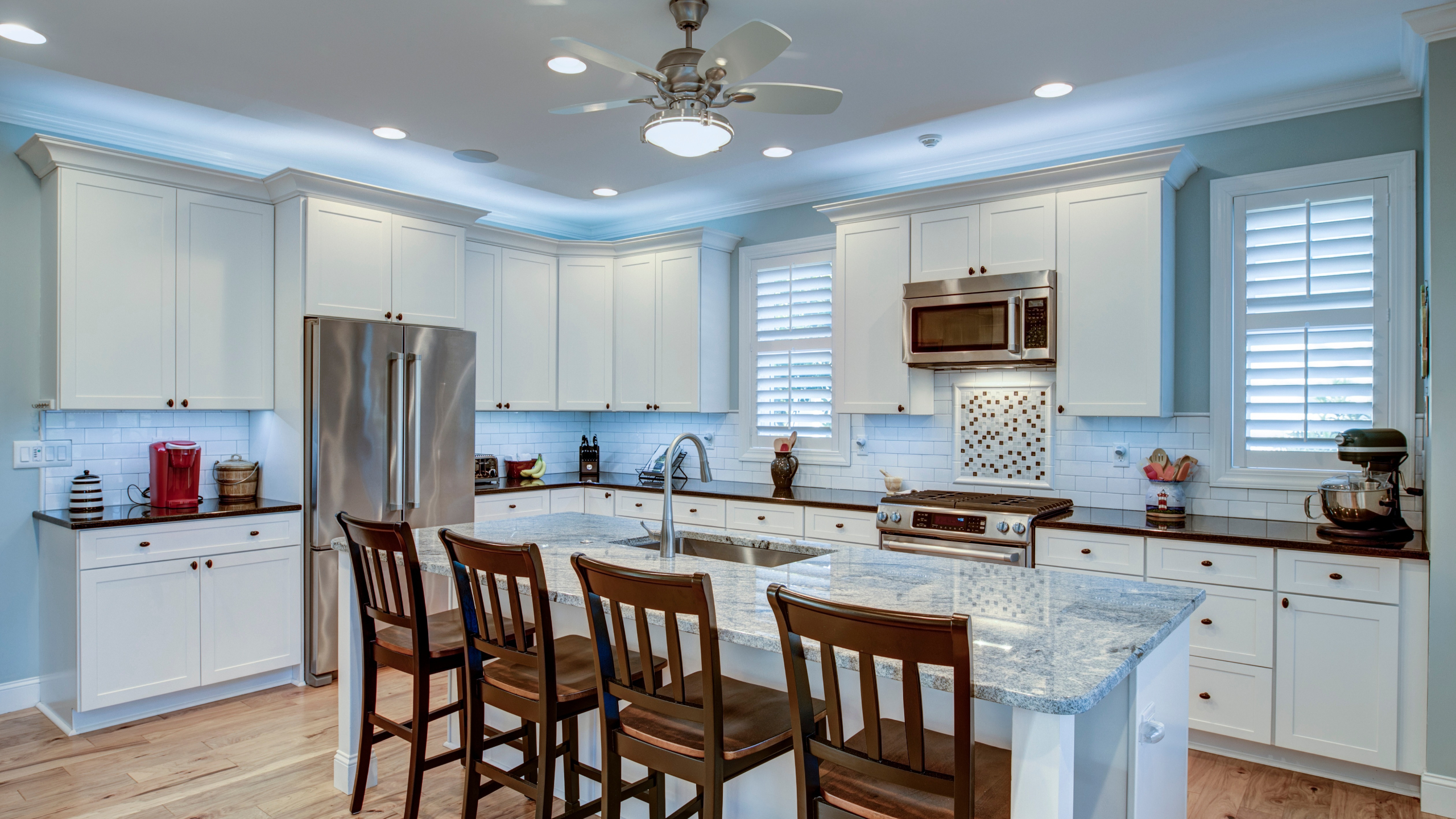 All-white kitchen with an island and silver appliances, and brown wood chairs