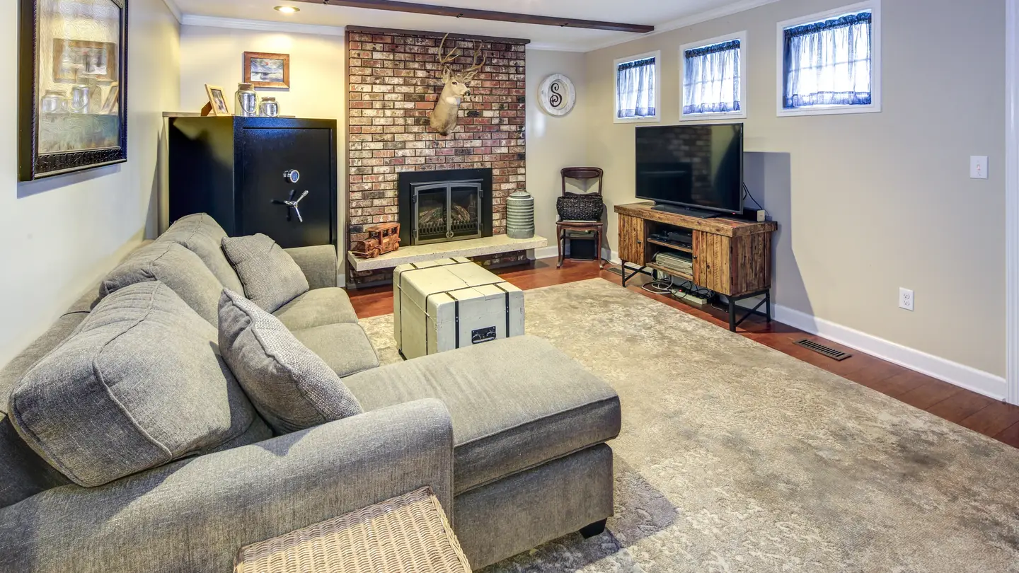 Finished basement with furniture and a safe with a brick fireplace and three windows.