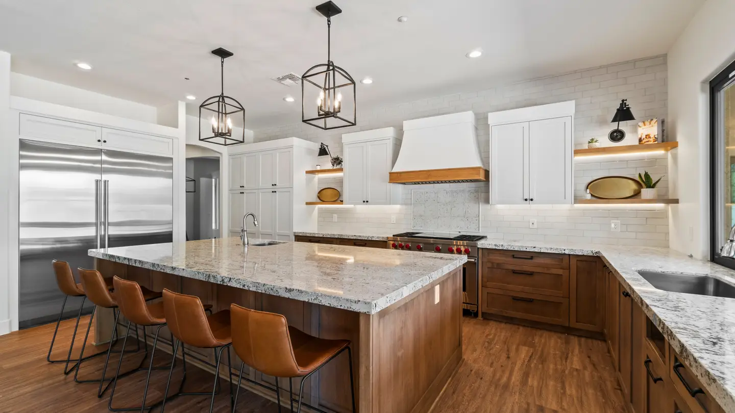 Kitchen with white and brown cabinets and an island in the middle with a granite countertop and black lights hanging over it.