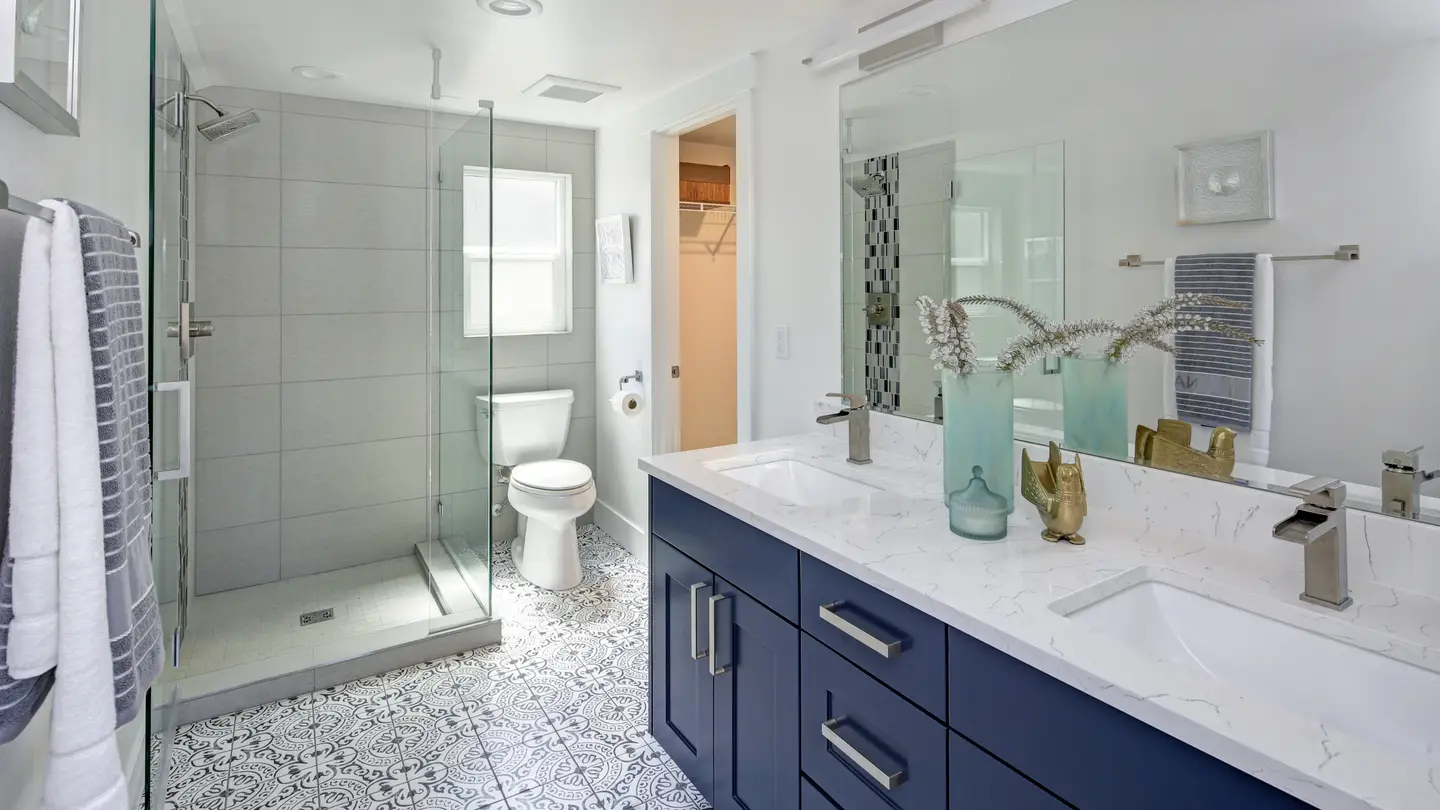 Bathroom with walk-in shower and gray and white tile floor with a blue vanity with a white countertop and a mirror.