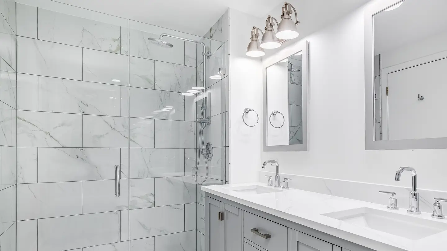 Bathroom with large, white walk-in shower and a light gray vanity with a white countertop and lights hanging over two mirrors