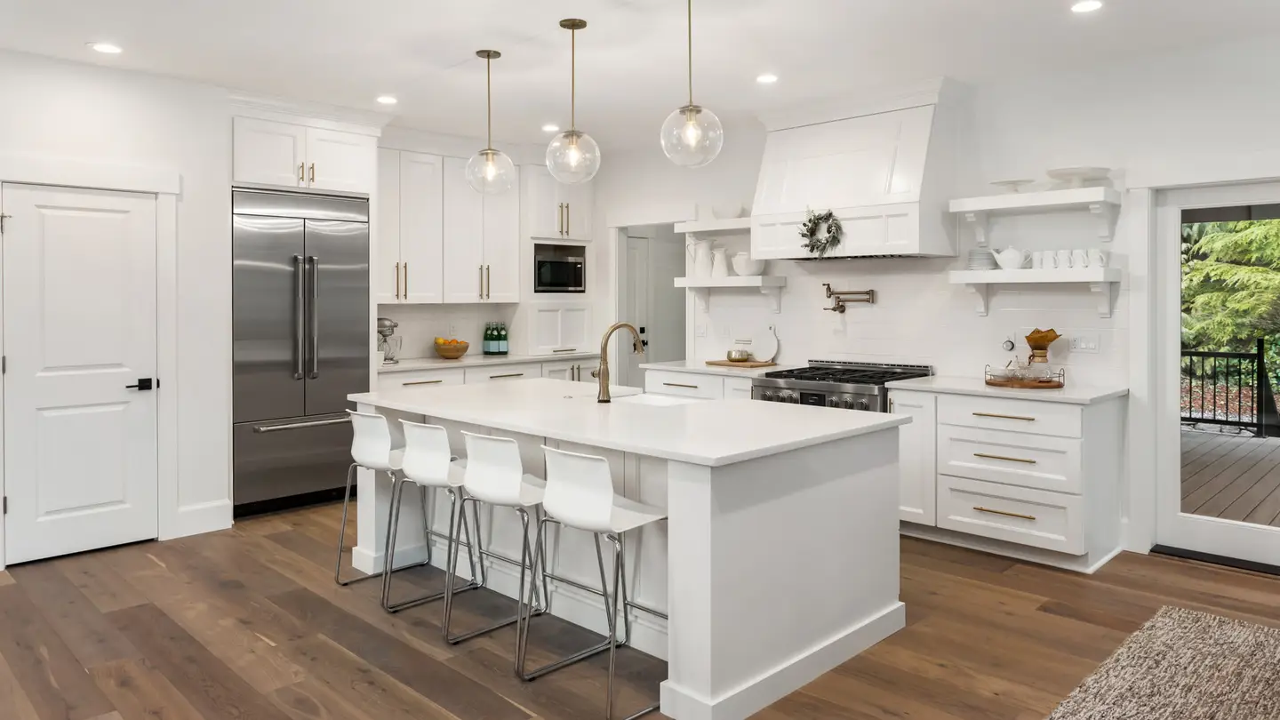 All-white kitchen with a white island and white chairs, and three lights hanging overhead
