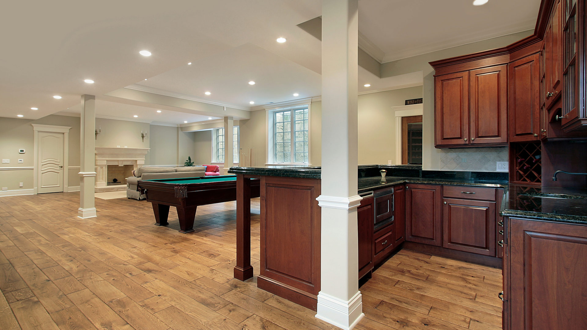 A finished basement with a kitchen in the corner and a pool table in the middle