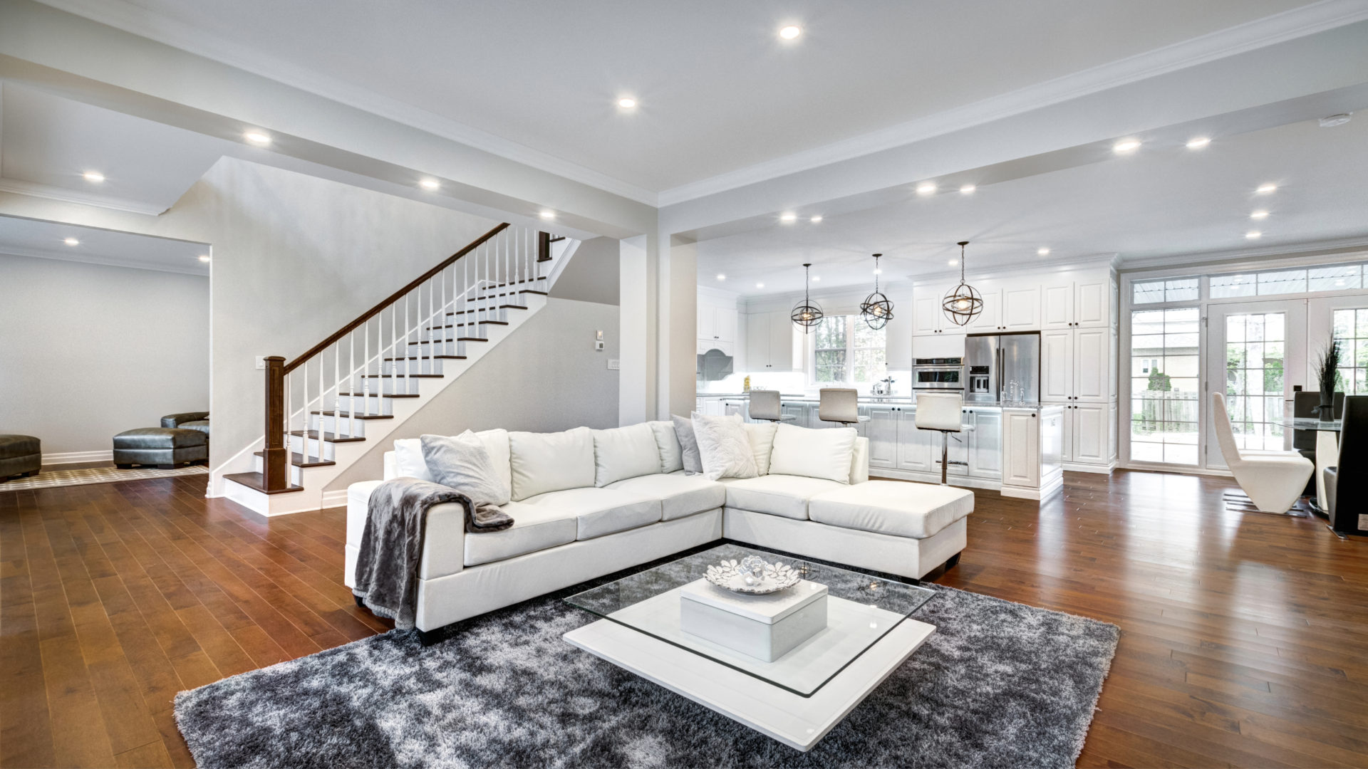 A basement with white walls and wood floors that has white furniture and a gray patterned rug 