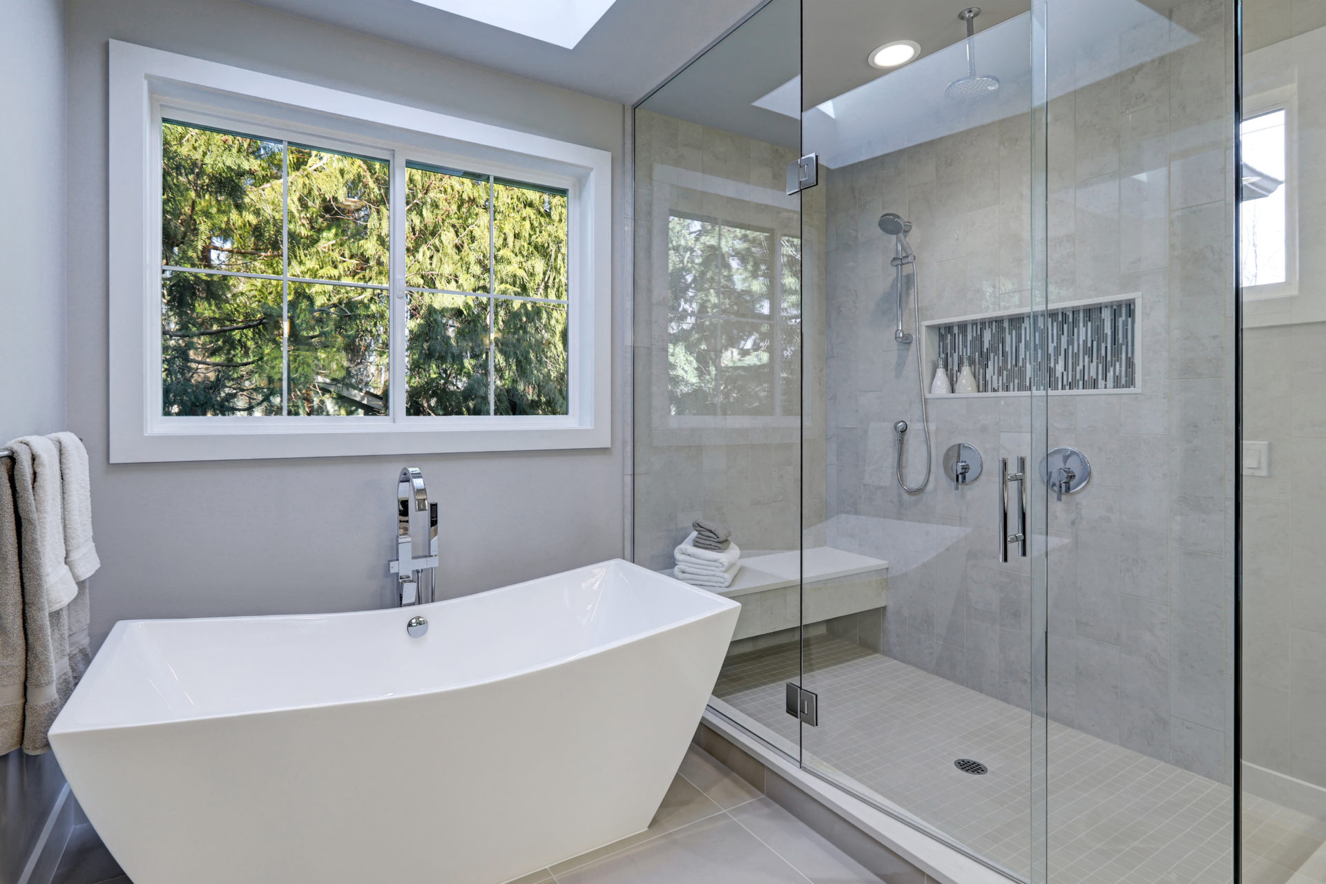 Bathroom with a white tub and a walk-in shower with glass and a window over the tu