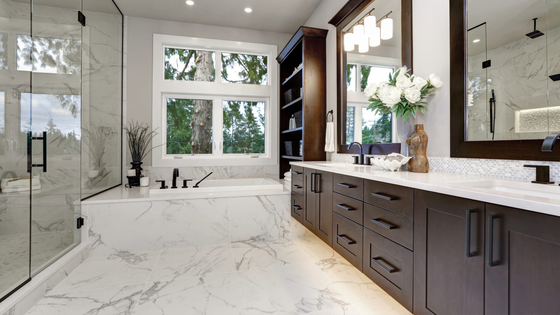 A large bathroom with a tub under a window and a large wooden vanity. The bathroom has white and gray floors 