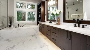 A large bathroom with a brown double vanity and a white and gray tub with windows over it