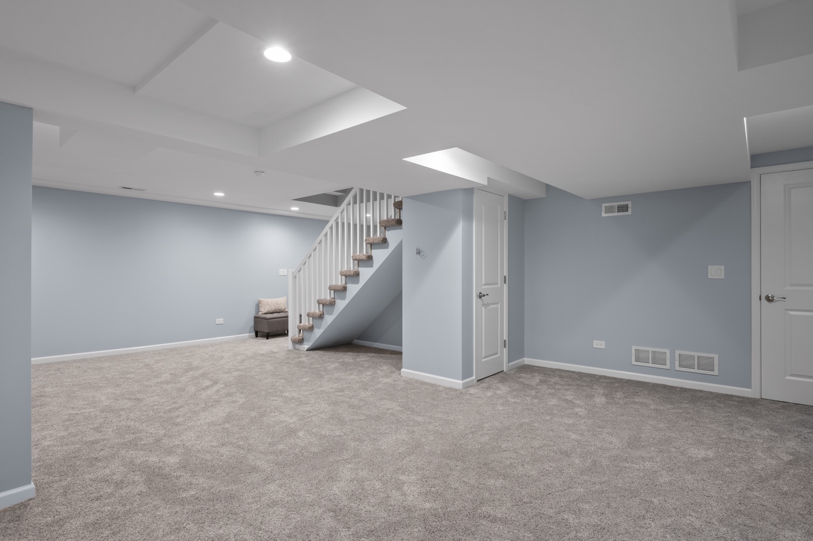 An open basement with light blue walls and white trim with a staircase with white rails