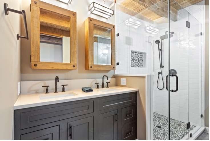 A compact bathroom with white tile walls, wooden mirrors above the sink, and a clear glass shower door.