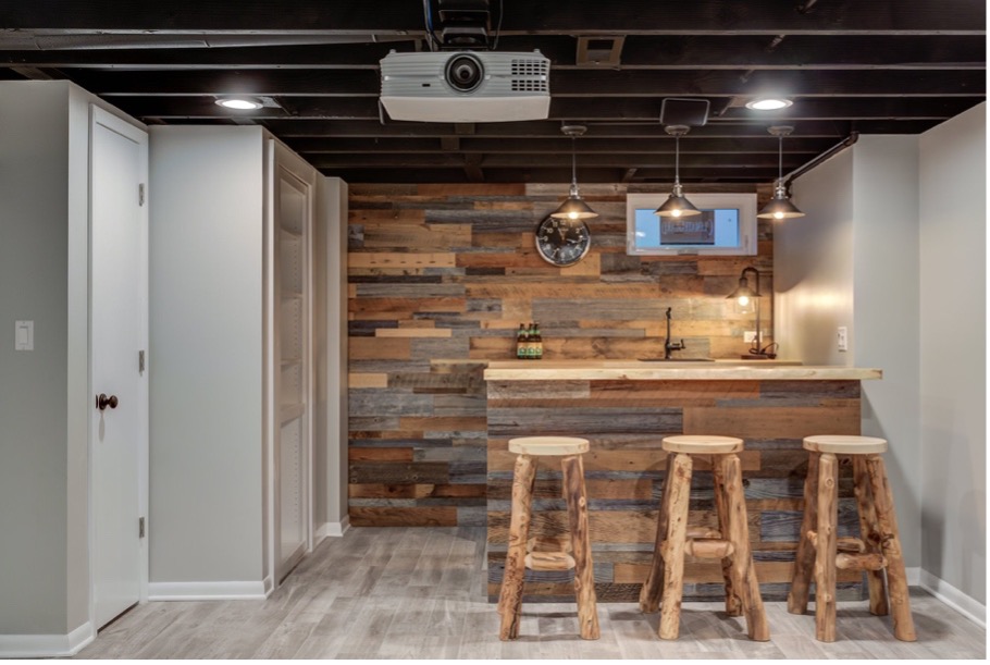 An open basement with white storage closets, a wood panel accent wall, and a bar with wooden stools