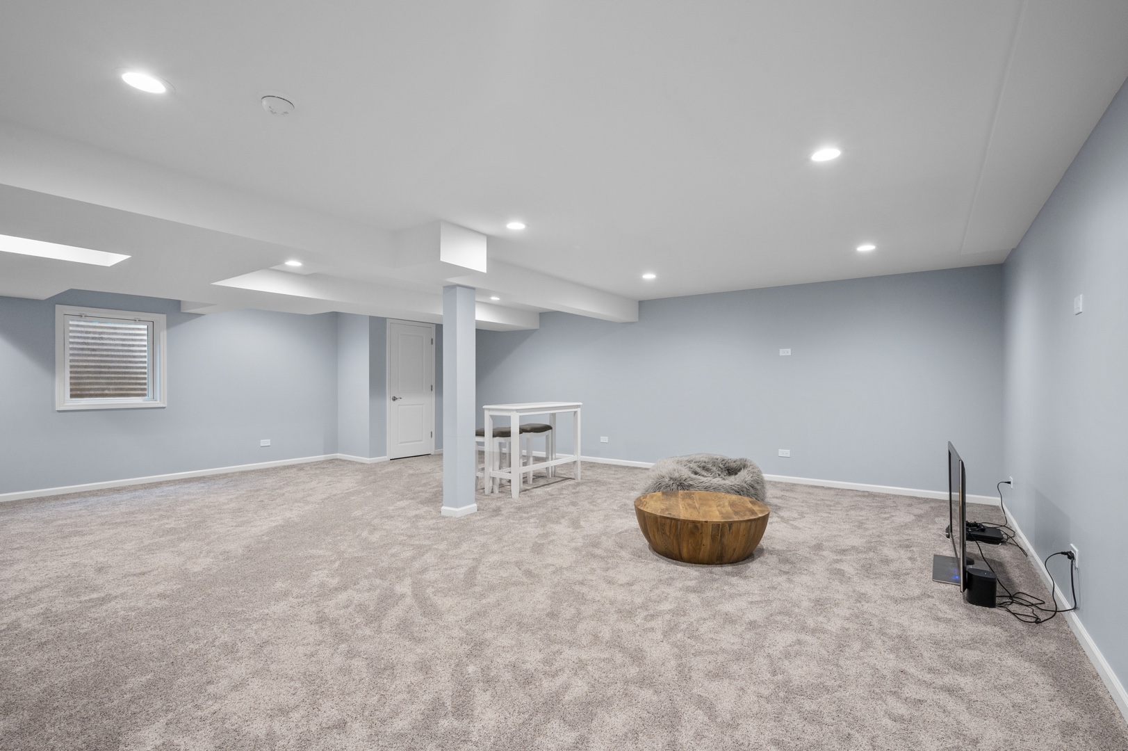 An open basement with white and blue walls, center beams, and bright recessed lighting