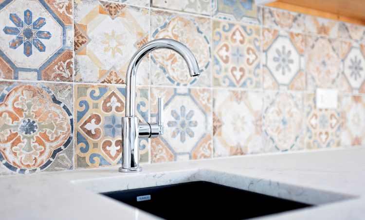 A newly remodeled kitchen with vibrant tiles behind a silver faucet.