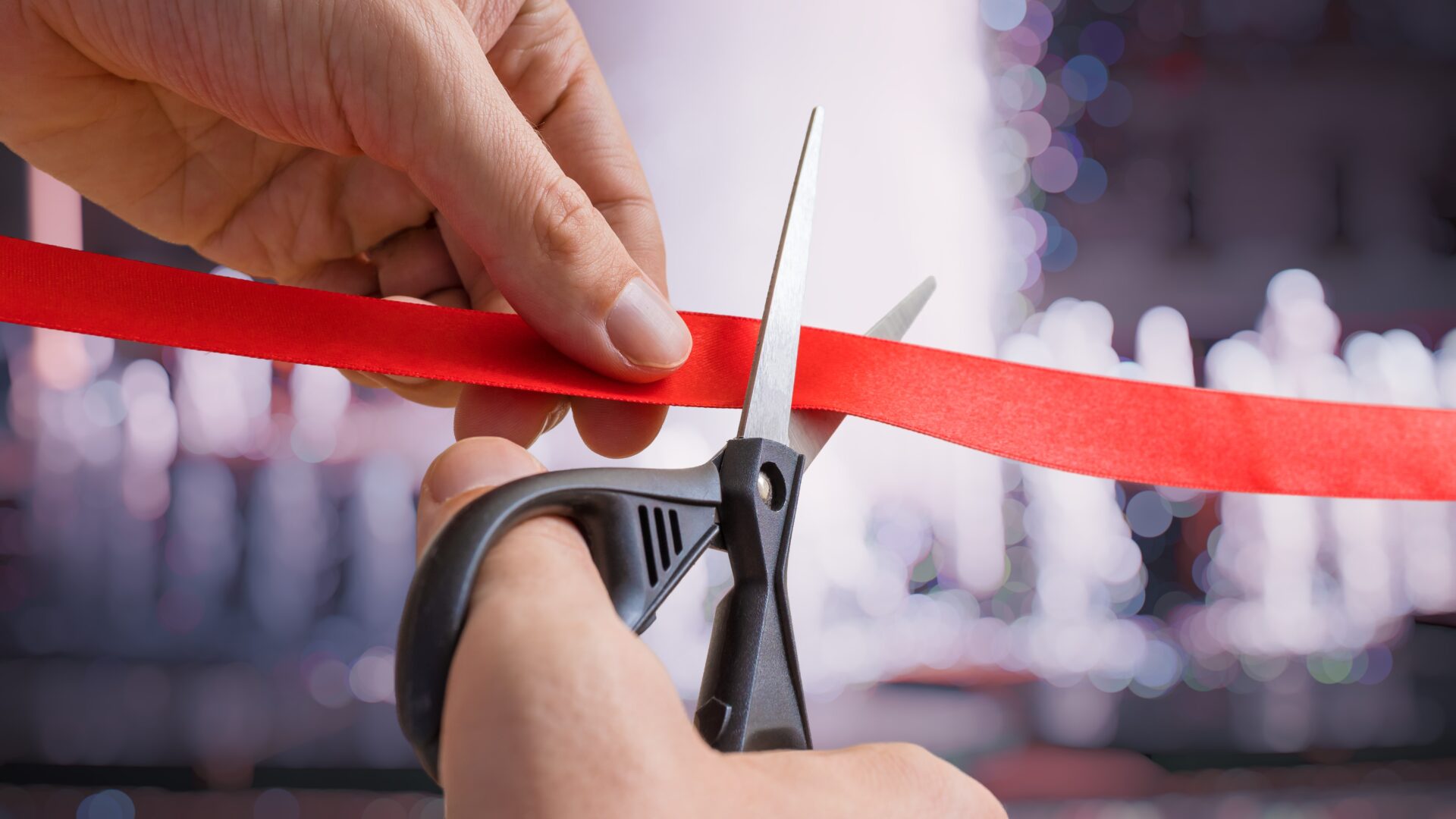 A man’s hands are cutting through red tape with scissors. The background is defocused.