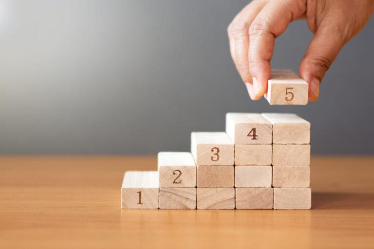 Women hand putting a wooden block on top and arranging wooden blocks stacking on wooden table  in the shape of a staircase, Business concept for growth success process.
