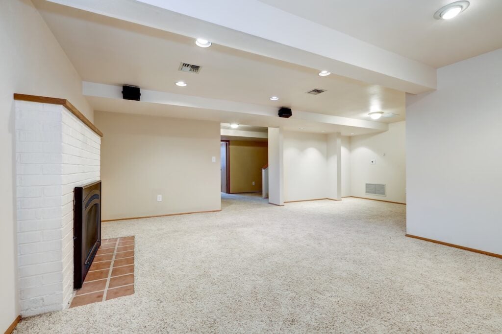 White empty basement room with fireplace and wall to wall carpet floor