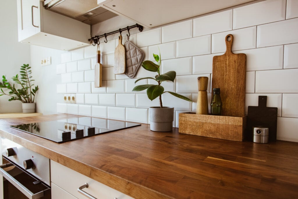 Kitchen brass utensils, chef accessories. Hanging kitchen with white tiles wall and wood tabletop.Green plant on kitchen background side view